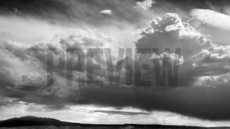 A black and white stock photograph of clouds over the desert landscape.